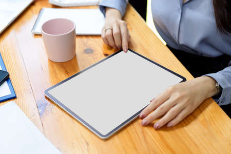Digital tablet blank screen mockup on wooden worktable, businesswoman using tablet, online websiteの写真素材