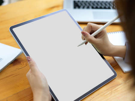 Closeup, female using stylus and digital tablet with blank screen mockup on working deskの写真素材