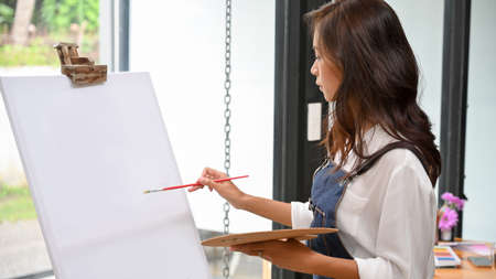 Blank canvas easel mockup for your artwork painting by attractive female artist, holding colour paletteの写真素材