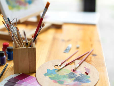 Closeup, side view, Artist painting tools, paintbrushes, colour palette, colour swatch sample, acrylic colour on wooden tableの写真素材