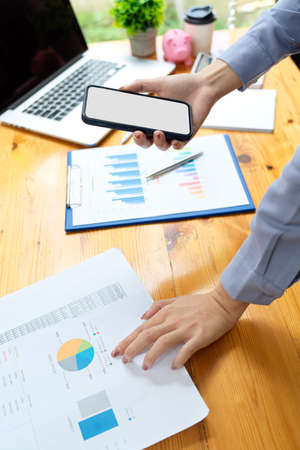 Close up, Businesswoman comparing business data from smartphone with financial report on desk, smartphone blank screen mockupの写真素材