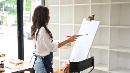 Creative female painter paints picture on canvas easel in her studio. blank canvas mockupの写真素材