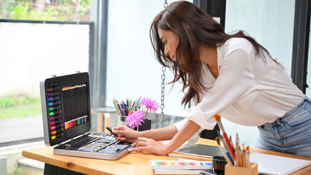 Image of Attractive female graphic designer leaning on table, choosing colour for her artwork projectの写真素材