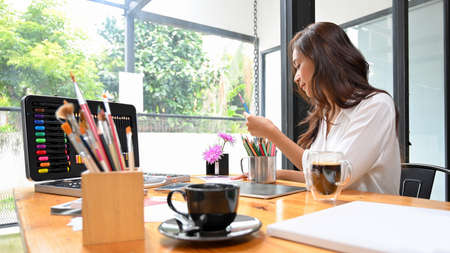 Female designer choosing colour pencils for her artwork, painting supplies on desk, creative...
