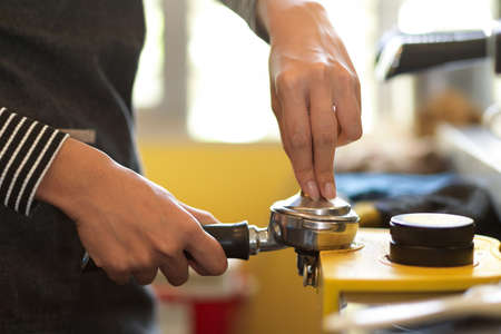 A female barista holding coffee tamper and porta filter with a coffee, pressing ground coffee for brewing at coffee shopの写真素材