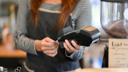 Cropped shot, Female barista taking credit card out of payment terminal, contactless payment, credit...