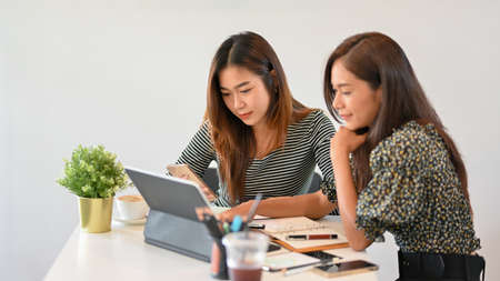 Two female designer working together, sharing idea, using portable tablet to find inspiration, creative occupationの写真素材