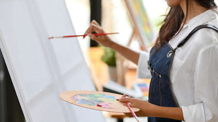 Closeup of painter artist painting on canvas easel, holding colour palette at art studioの写真素材