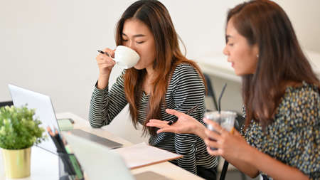 Asian young businesswomen working with laptop computer and drinking coffee at cafe co-working space,...