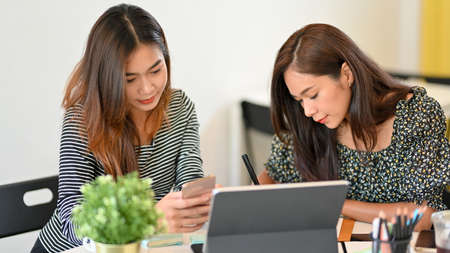 Young businesswomen working together, using smartphone, browsing information on internet, tablet and office supplies on deskの写真素材