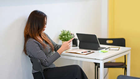 Woman using smartphone, chatting with friends, browsing internet, relaxed after work at cafeの写真素材