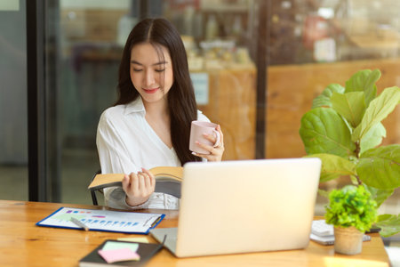 Attractive businesswoman reading book, sitting at coffee shop, relaxed female entrepreneurの写真素材