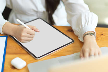 Cropped image of businesswoman using digital tablet with stylus pen on worktable, tablet blank screen mockup, designer sketching design on graphic tabletの写真素材