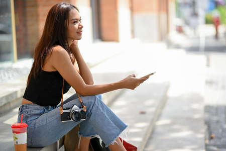 Asian woman shopping in sunny day concept, sitting on stairs outside of the mall, holding mobile...