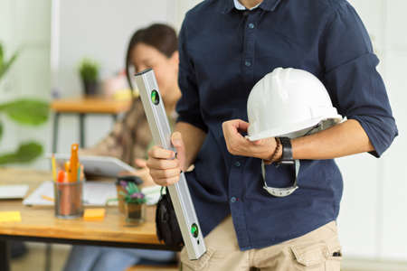 Cropped image of male construction engineer with hardhat and spirit level standing in engineering officeの写真素材