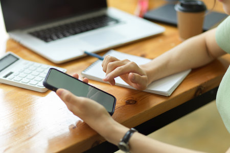 Close up, Young female officer using smartphone to contact business client at office desk, female accountant using mobile phoneの写真素材