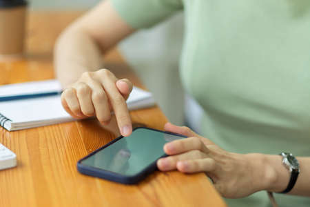 Woman's hands using mobile phone on work table at home, businesswoman searching information via smartphone, close upの写真素材