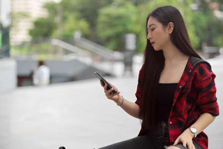 Beautiful young woman using smartphone in city street, holding mobile phoneの写真素材