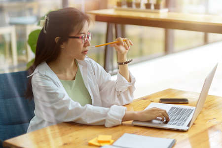 Female engineer with eyeglasses pensive thinking about her project on laptop computer, measuring...