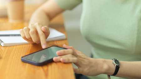 Close up, young woman using smartphone, putting mobile on wooden table, touching mobile screen,...
