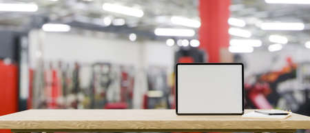 Mockup space on wooden tabletop with blank screen tablet mockup over blurred fitness gym in the background, Technology and sport concept, 3d rendering, 3d illustrationの写真素材