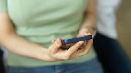 Closeup young female in pastel green comfy shirt sitting and holding mobile phone, using smartphone in living room at home, chilling and relaxingの写真素材