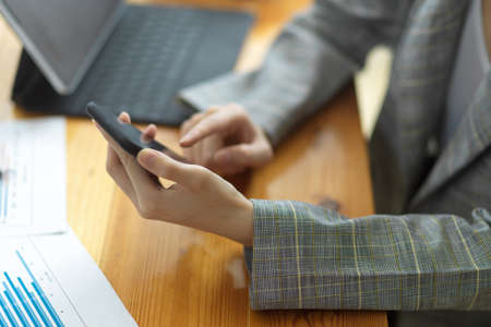 Cropped image of female entrepreneur or businesswoman browsing on internet via smartphone at her desk. text email for negotiate with business clients. working on mobile phoneの写真素材
