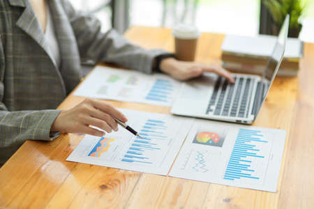 Closeup, Female manager checking business sale data on papers. laptop and report on desk, pen pointing on paperworksの写真素材