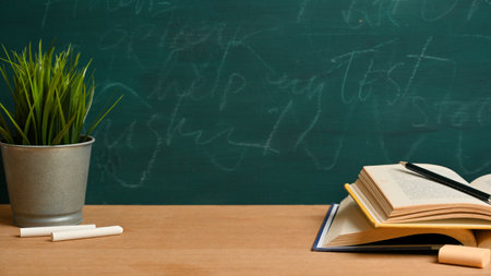 Mockup space on wooden table with opened books, pencil, chalks, plant over green blackboard. Classroom or school conceptの写真素材