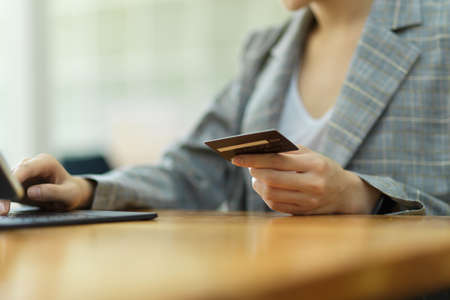 Cropped photo of Hand holding credit card and using tablet. Businesswoman or entrepreneur working in office. spending money, online payment, paying billsの写真素材