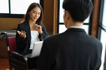 Beautiful disabled businesswoman meeting with her boss in boardroom. Office girl in wheelchair
