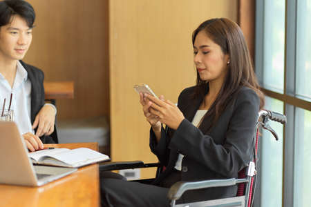 Businesswoman in wheelchair relaxing on smart mobile phone after finished meeting in meeting roomの写真素材