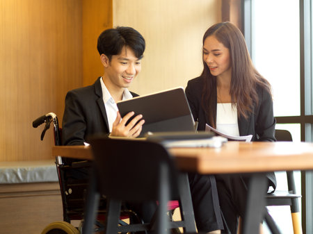 Happy businessman and businesswoman talking about their new project in office. Businessman in wheelchairの写真素材