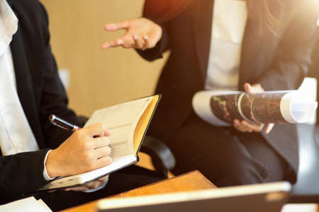 Cropped shot of Executive businesswoman sitting at desk giving business strategy advice to her young assistant. Businessman taking notes on personal agenda bookの写真素材