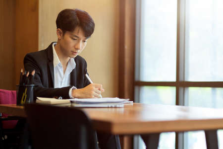 Young asian businessman sitting and writing business project on paper in officeの写真素材