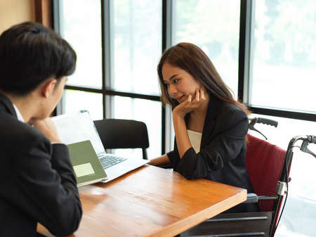 Friendly businessman having a good conversation with female employee in wheelchair. Businesswoman in...