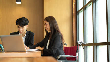 Image of businesswoman in wheelchair meeting with her boss in meeting room. Disabled person in workplaceの写真素材