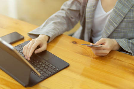 Crop image of female freelancer holding credit card and typing on tablet keyboard for buying online goods, transfer moneyの写真素材