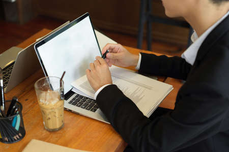 Closeup, Young asian businessman in black suit working on laptop computer with data spreadsheets on keyboard in co-working space. laptop blank screen mockupの写真素材