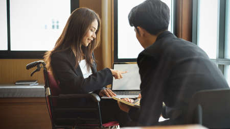 Attractive asian businesswoman in wheelchair working with colleagues in office, discussing project...