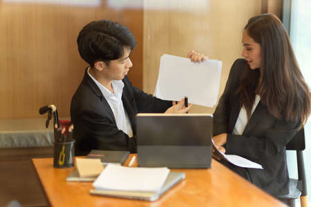 Disabled businessman presenting his work in online meeting via digital tablet with his female partner in office. man in wheelchairの写真素材
