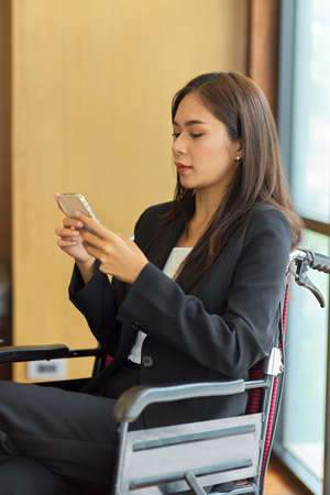 Female in wheelchair using smart mobile phone in office. Disabled business personの写真素材