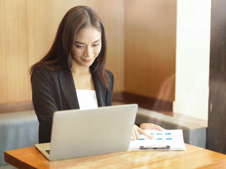 Confidence businesswoman working on laptop and reviewing financial report in officeの写真素材