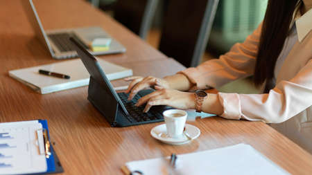 Cropped image of a businesswoman working on a portable tablet, a female assistant typing on the keyboard while the company meets in a meeting room.の写真素材