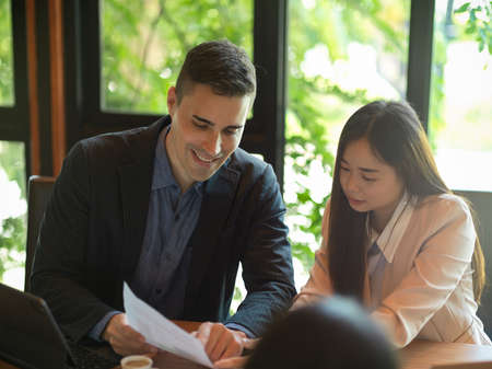 Image of happy caucasian businessman explaining new marketing strategy to his asian colleagues in conference roomの写真素材