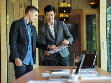 Two businessmen working together in a meeting room, looking at a financial report graph for forecasting business budget. diverse business peopleの写真素材