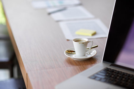 Close up image of laptop computer and coffee cup on wooden table with paperworks in conference roomの写真素材