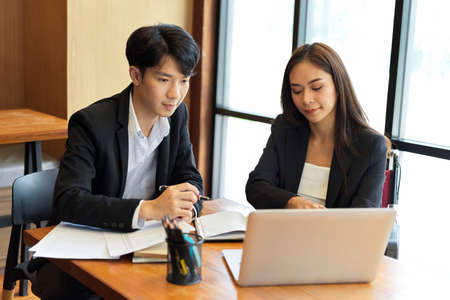 Two business professionals working on a laptop computer together, a businessman and a businesswoman, teamwork, brainstorming, and idea sharingの写真素材