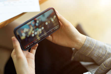 Female is watching a video on her smart phone while holding it horizontally. bokeh video, enjoyment, relaxationの写真素材