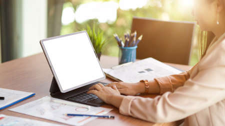 Female accountant working on digital tablet in her work station. tablet blank screen mockup and business report on deskの写真素材